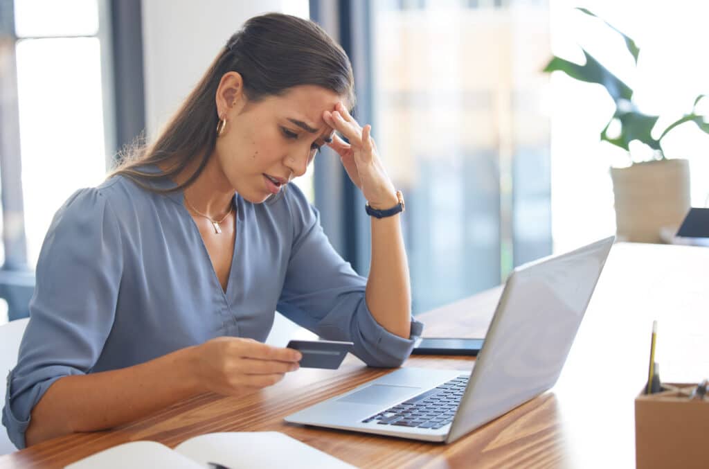 woman looking at bank card and laptop after experiencing bank fraud