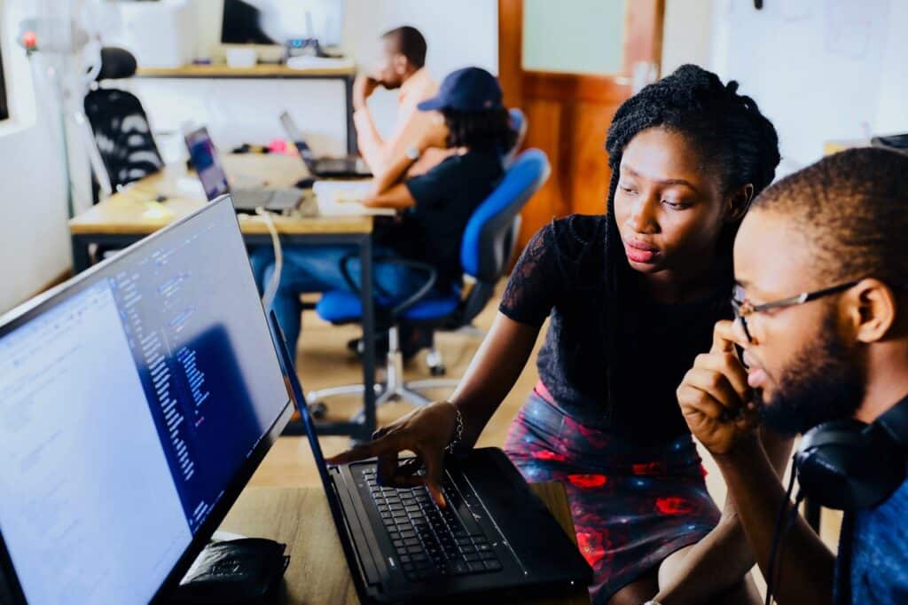 Two people sit next to each other and look at a computer