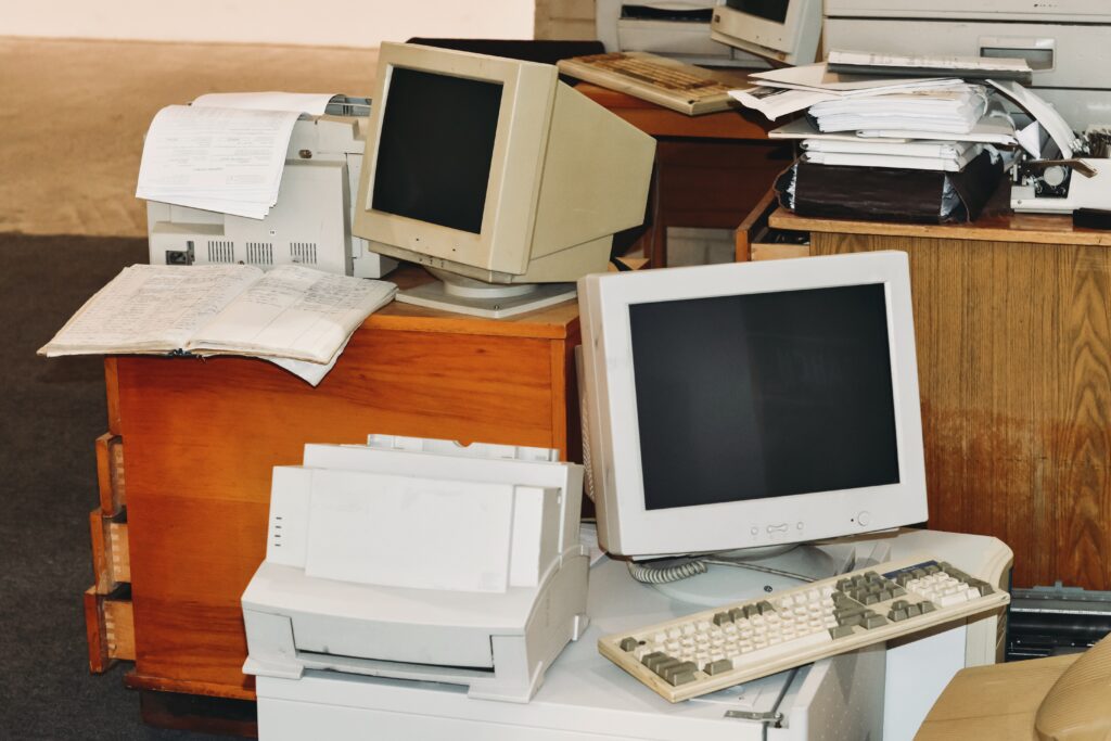 Old, end of life computers, printers, typewriters, and keyboards on table and floor